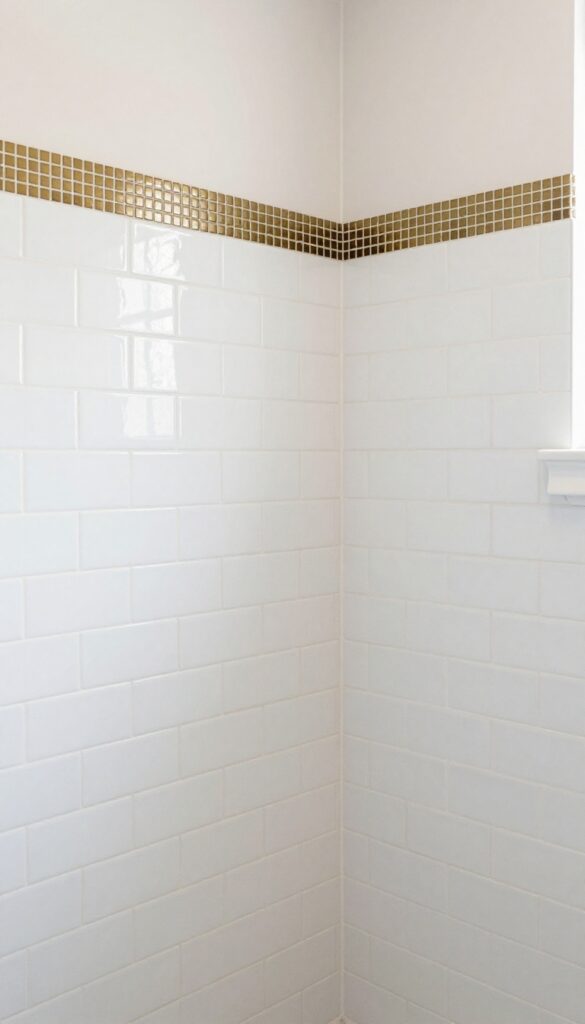 A modern shower with layered tile borders featuring a brass mosaic strip above white subway tiles, adding dimension and elegance in bright natural light.