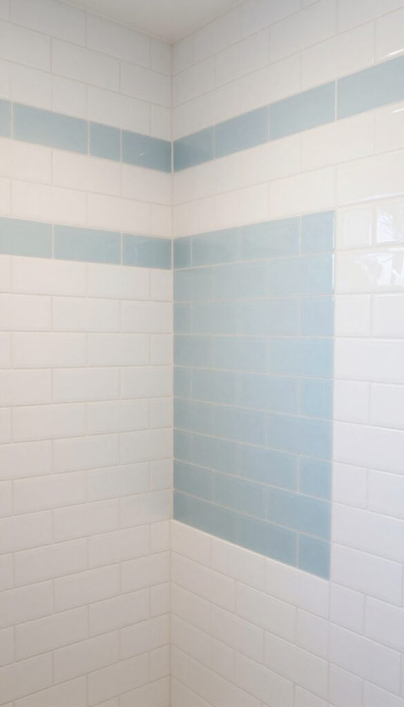 A shower wall with white subway tiles and soft blue glass tile accents in natural light.