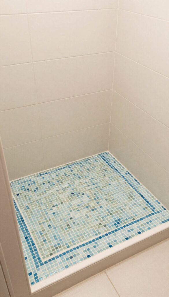 A shower seat with mosaic tile accents in soft blues and greens, adding artistic flair to a bright bathroom.