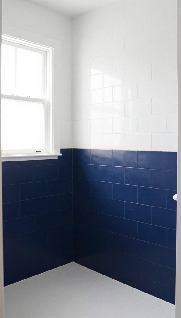 A bathroom shower featuring a knee wall painted in contrasting deep navy against white subway tiles, illustrating color blocking for modern structure without closing off the space.