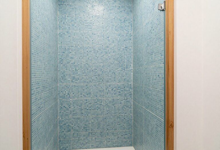 Coastal bathroom shower with textured blue mosaic tiles and wood accents in a bright, airy setting.