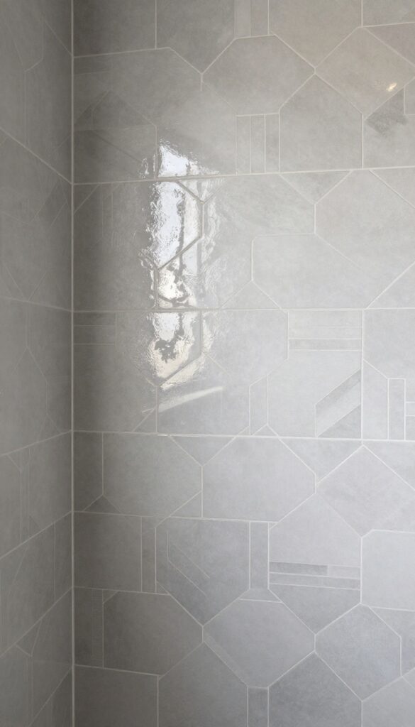 Geometric pattern shower wall with alternating glass and ceramic tiles in hexagon or chevron shapes under bright natural light.