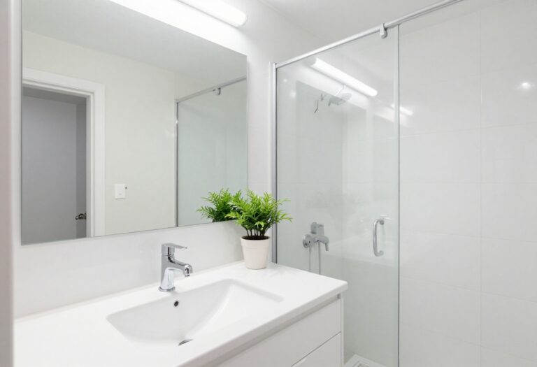 A clean, bright bathroom with white tiles, a modern vanity, and a small plant on the counter, reflecting a fresh weekly reset.