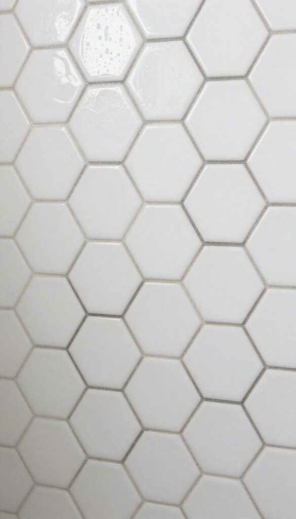 Matte white hexagon mosaic tile shower floor with dark grout, wet texture, natural light
