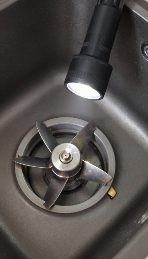 Close-up of a garbage disposal chamber with a flashlight revealing a hidden food trap near the impeller blades