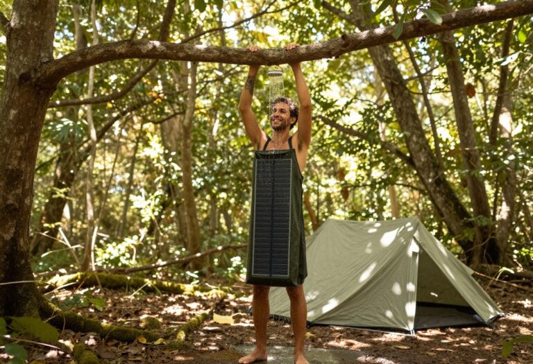 Person taking a DIY camping shower in a forest with a solar shower bag and privacy tarp